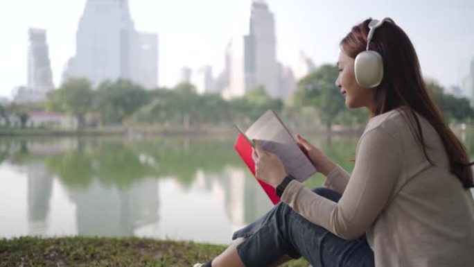 亚洲女性很高兴早上在城市公园听音乐和看书，人们在城市自然环境中放松身心。