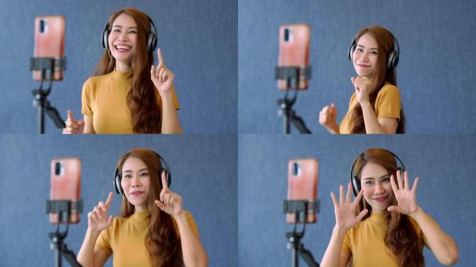快乐的年轻亚洲女性美丽的博客作者使用耳机并在智能手机上录制视频以进行社交媒体应用。自由和积极的生活方