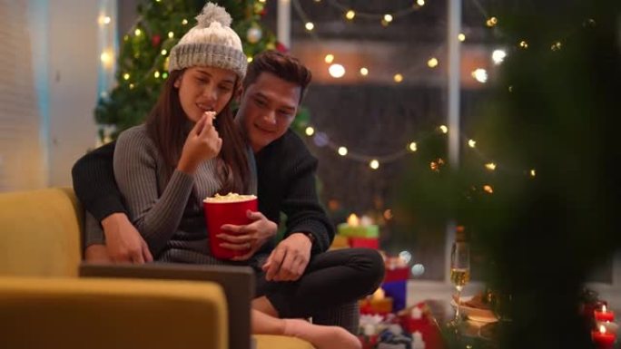 亚洲夫妇坐在沙发上吃爆米花。圣诞夜和新年季节的浪漫恋人。