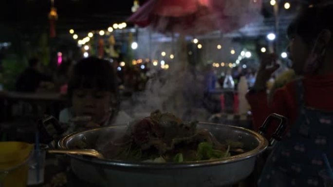 炉子上烤猪肉，泰国菜自助餐。双手握着筷子在热锅上烧烤传统的泰国风味烧烤，包括猪肉，大虾，牛肉，鸡肉，