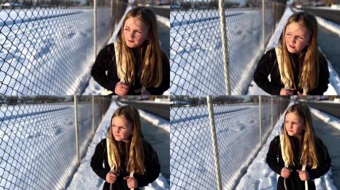 8-10岁的女孩正在考虑在小学附近的铁丝网围栏旁远离相机
