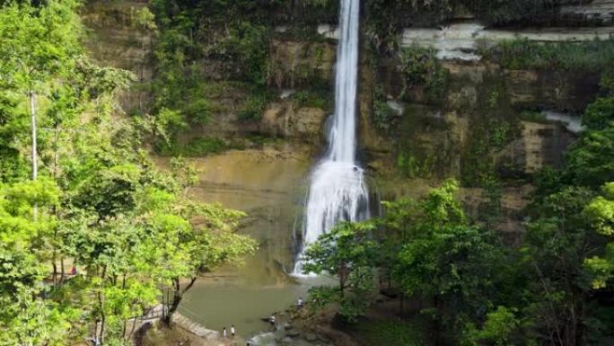 一个美丽的小瀑布的鸟瞰图。无人机远离瀑布，瀑布是一个深受旅行者欢迎的旅游景点。在许多绿树和令人惊叹的