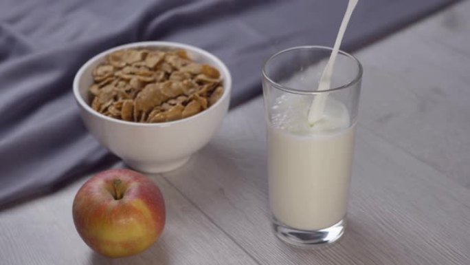 将牛奶倒入木制桌子上的玻璃杯中。早上健康早餐。谷物、水果和牛奶