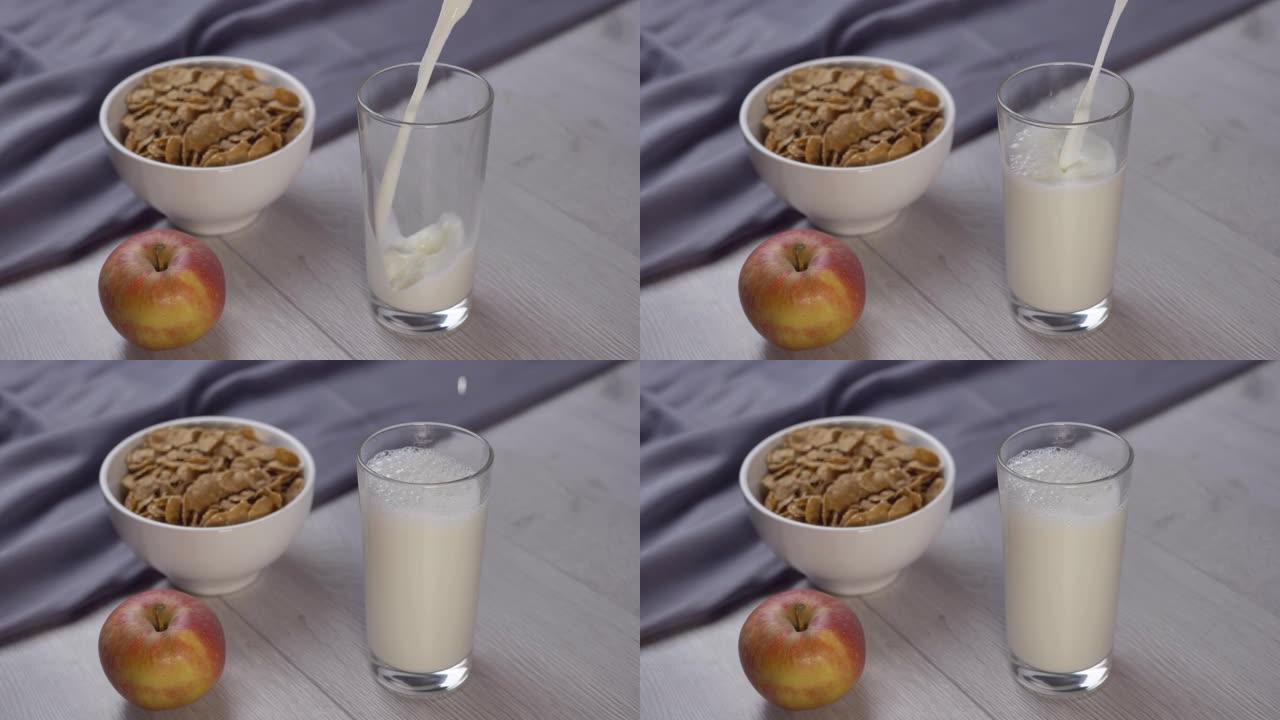 将牛奶倒入木制桌子上的玻璃杯中。早上健康早餐。谷物、水果和牛奶