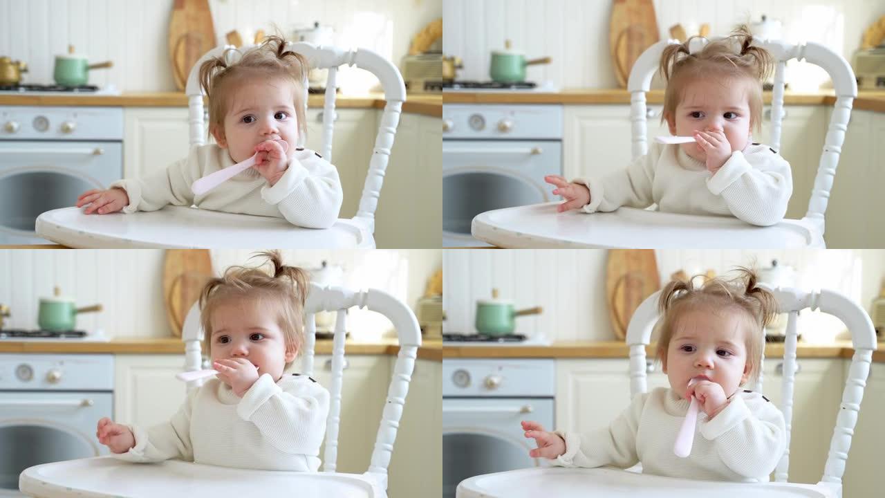 婴儿坐在高脚椅上在厨房里喂食，等待午餐吮吸塑料勺子。第一次尝试吃固体食物，成长