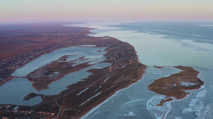 寒冷的冬日日落时海滨小镇的鸟瞰图。海岸有岛屿、湖泊和海湾。冰冻大海附近的定居点。冬季海岸村庄的夜灯