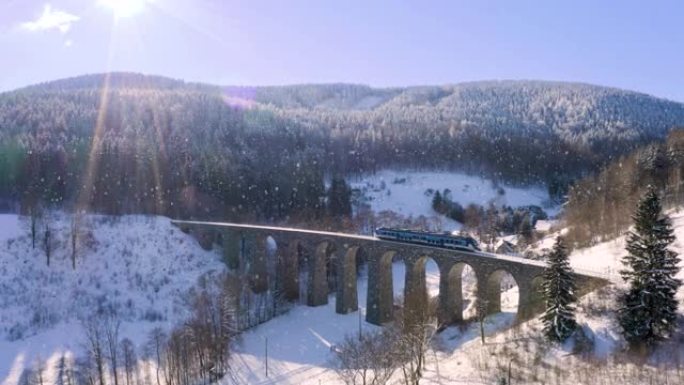 旅客列车在飘落的雪中穿过一条石制铁路高架桥，变焦。