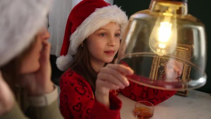 穿着圣诞服装的高加索小女孩在家里度过圣诞节，看着一站复古灯泡