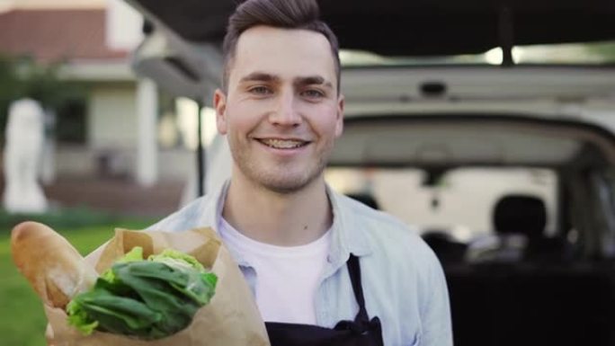收起帅气的微笑，看着相机快递员从汽车到房子，在户外拿着装有蔬菜的纸袋