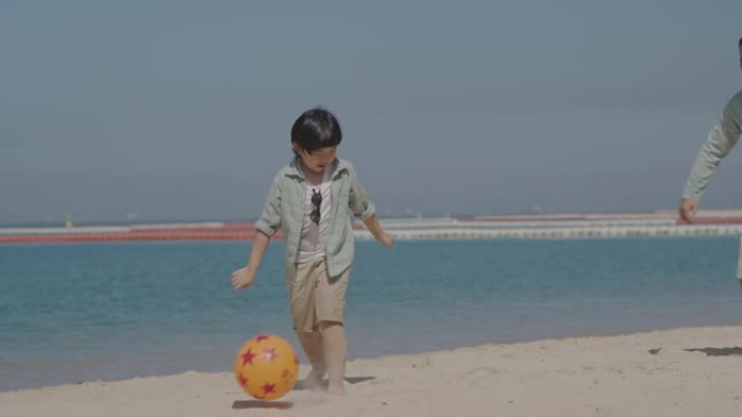亚洲父亲和儿子在海滩上踢足球。