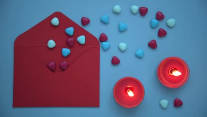 情人节时尚舒适的照片。从上方观看，在蓝色背景上摆放着信封，蜡烛和心形。一个红包，从中倒出心。燃烧的蜡