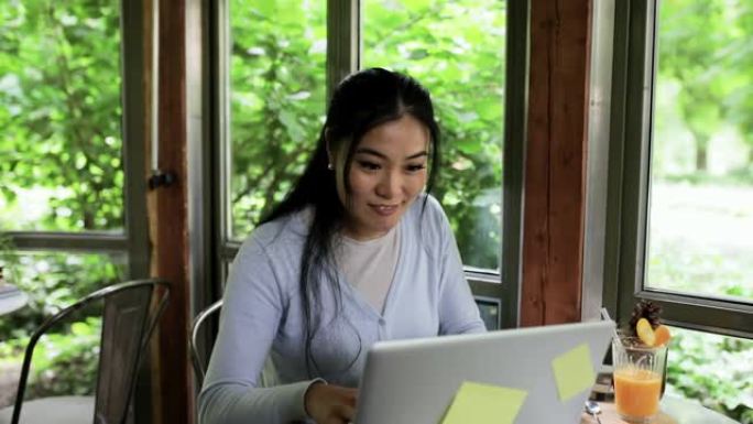 使用笔记本电脑在咖啡店工作的年轻亚洲女性。