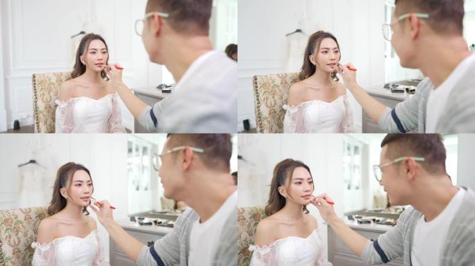 4k亚洲男化妆师为穿着白色婚纱的女性新娘化妆。