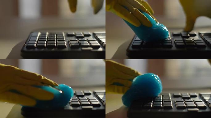穿着黄色手套的无法识别的年轻人的特写镜头使用蓝色粘液吸收凝胶，慢动作清洁和清除pc键盘上的碎屑。