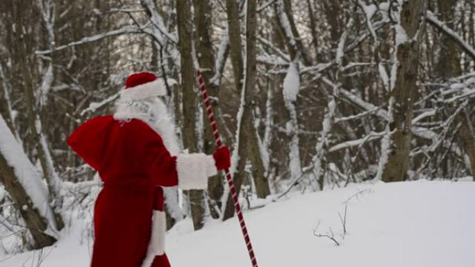 圣诞老人带着魔法杖和一袋圣诞礼物走在雪林里。