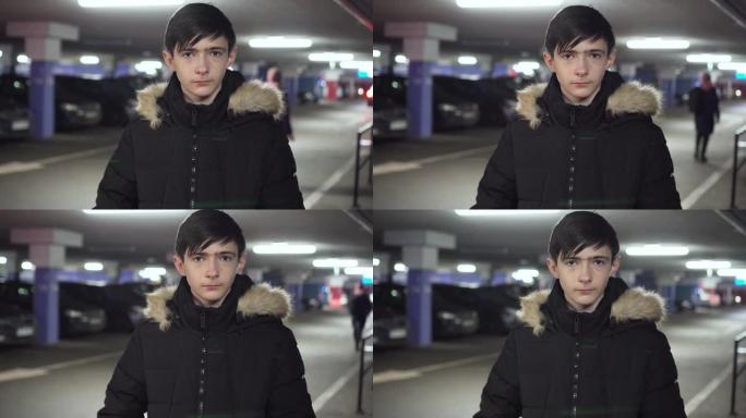 孤独悲伤的少年男孩站在黑暗城市的地下停车场，路过汽车，走在不同的人