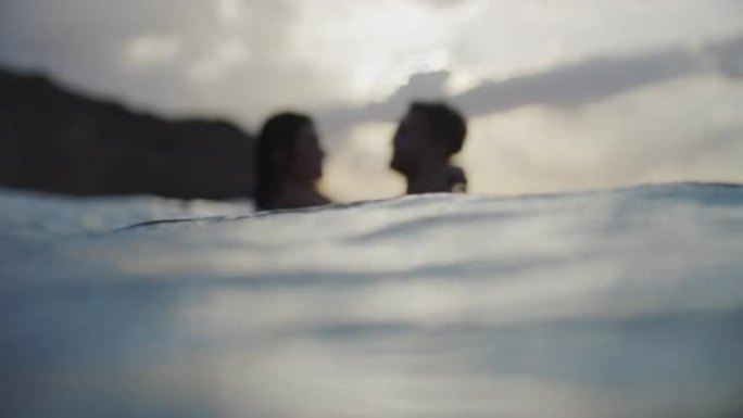 浪漫的异性恋夫妇在金色日落时在海里游泳。接吻和玩耍