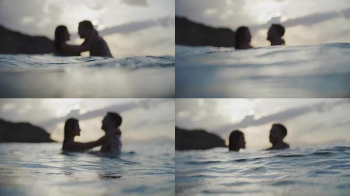 浪漫的异性恋夫妇在金色日落时在海里游泳。接吻和玩耍