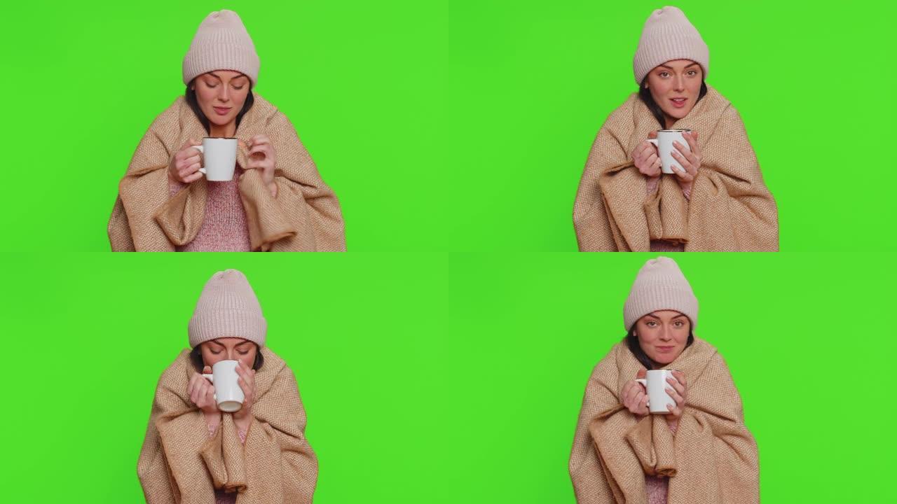 生病的女人戴着帽子裹在格子里独自冻得瑟瑟发抖，喝着热茶，试着热身