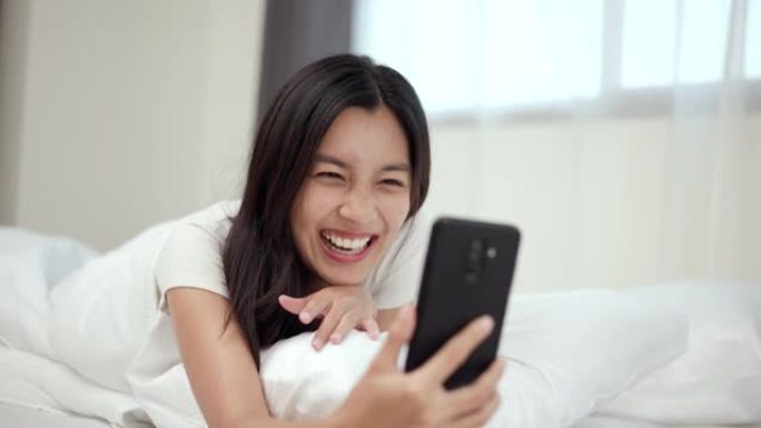 漂亮的亚洲女人在床上用智能手机在家打电话给社交媒体。年轻美丽女性的生活方式在睡觉前使用手机上网。