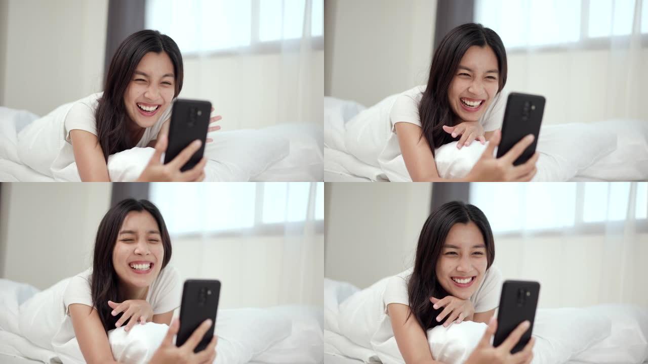 漂亮的亚洲女人在床上用智能手机在家打电话给社交媒体。年轻美丽女性的生活方式在睡觉前使用手机上网。