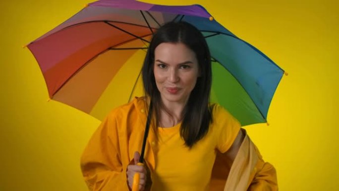 穿着黄色雨衣的迷人女人带着彩虹伞调情跳舞