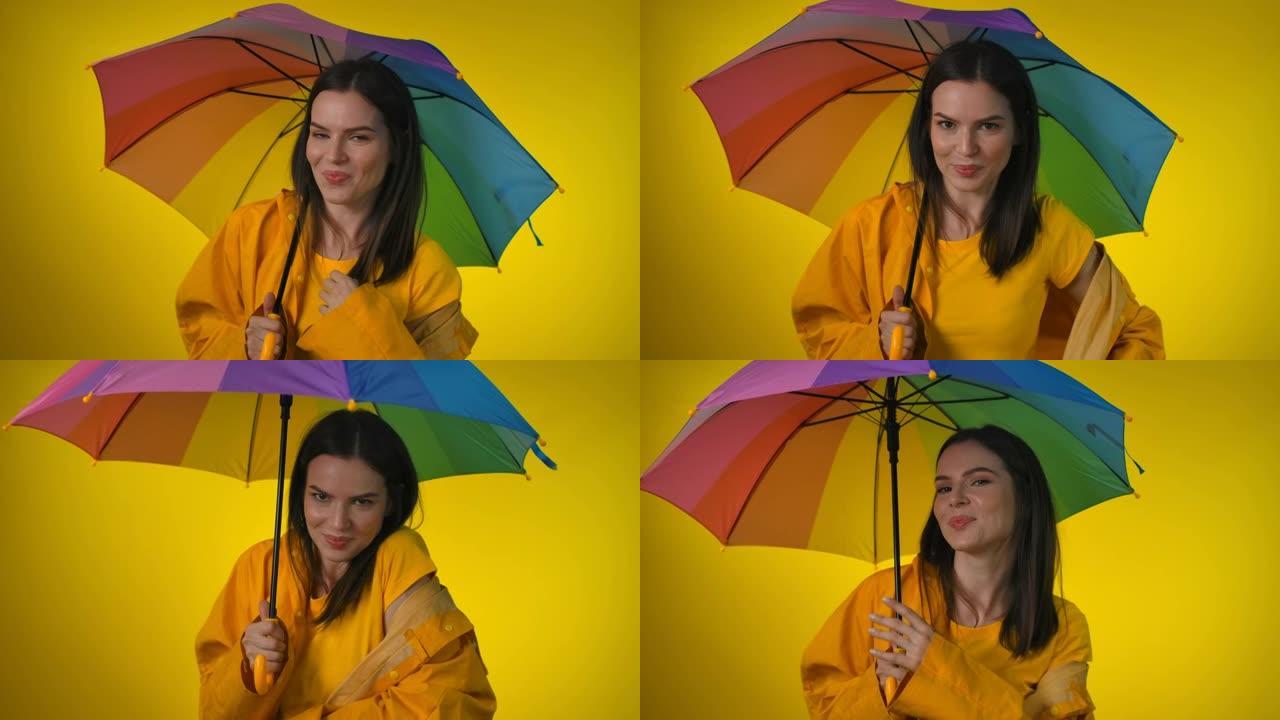 穿着黄色雨衣的迷人女人带着彩虹伞调情跳舞
