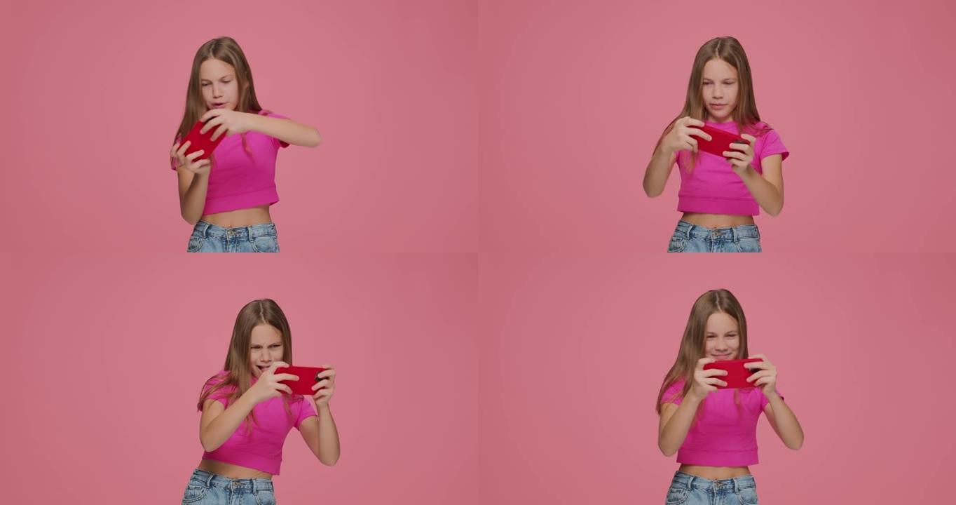 赌博小女孩Z世代游戏玩家孩子在粉红色工作室背景下的手机上玩在线虚拟游戏。小玩意成瘾