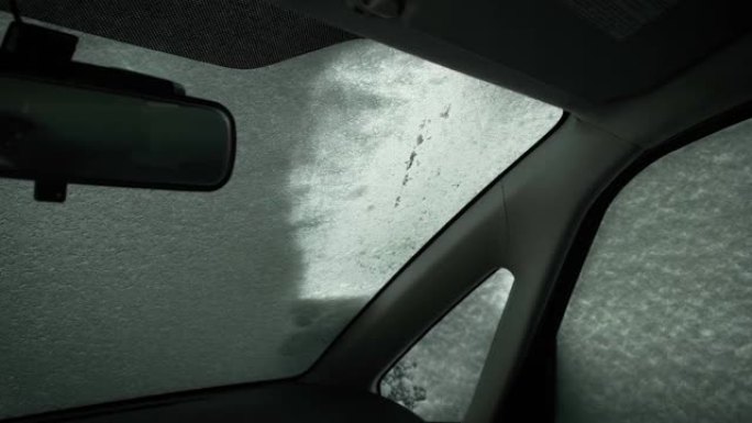 用刷子和废料从冰冻的挡风玻璃上清除冰雪的人。从车内观看。寒冷的冬季天气，自然灾害。暴风雪过后，男子打