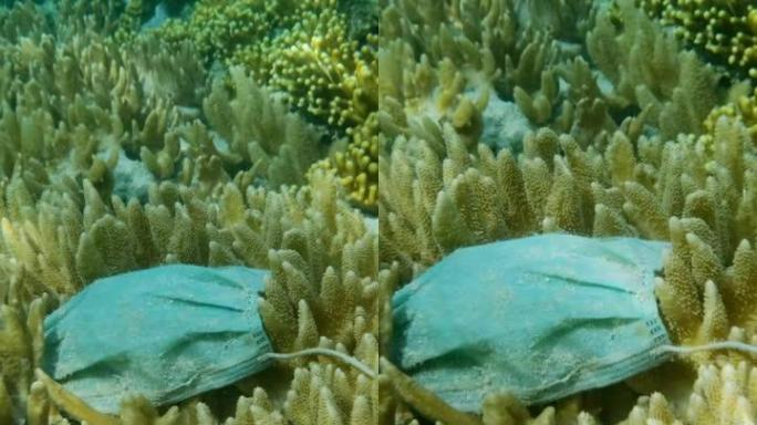 废弃的二手医用口罩的特写镜头位于阳光下美丽的柔软珊瑚的水下。海洋的污染面具。慢动作，摄像机向前移动