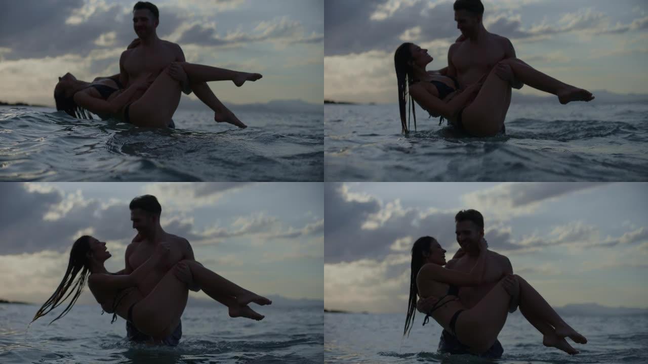 浪漫的异性恋夫妇在金色日落时在海里游泳。在水中玩耍