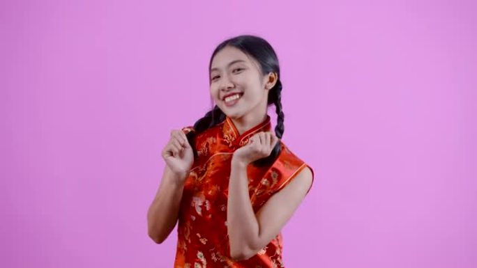 4K，扎着红色中国新年旗袍的中国血统的亚洲妇女，高兴地站着跳舞，竖起两个大拇指。微笑，开心，独自一人