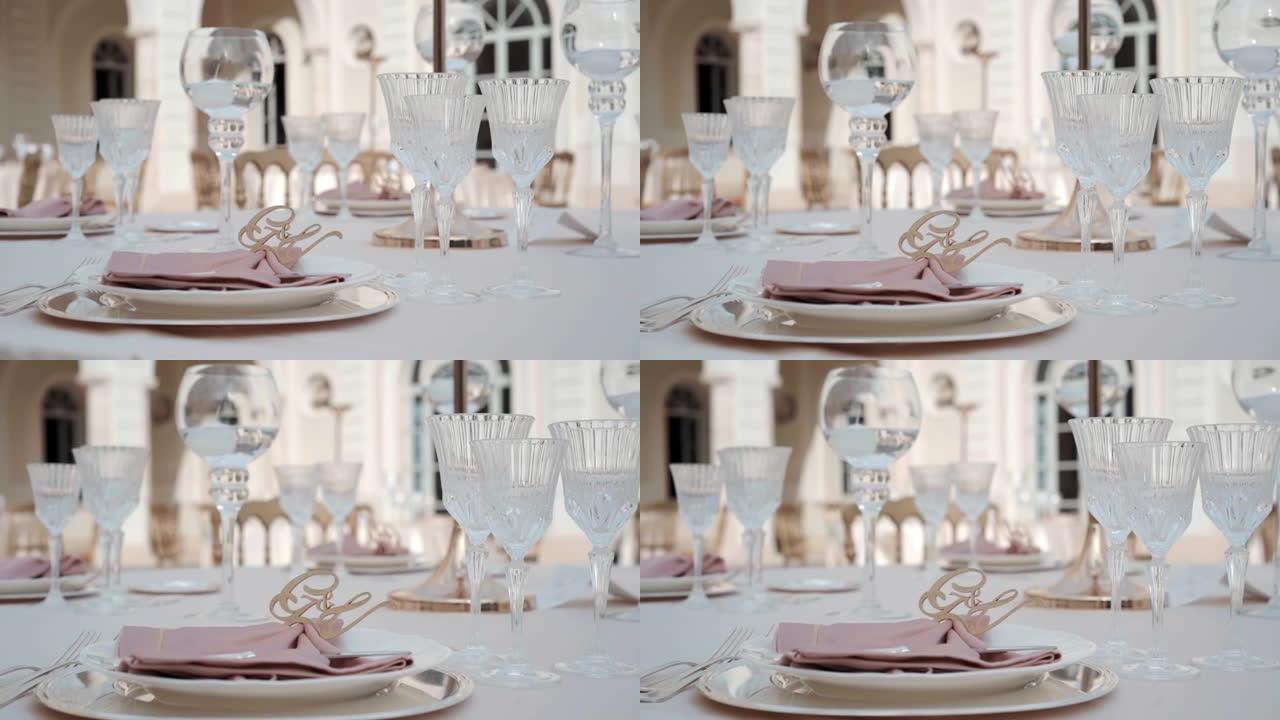 优雅的宴会桌设置为豪华的户外正式派对，水晶高脚杯装饰着蜡烛，酒杯和带有姓名字母的设计师餐巾纸。宴会餐