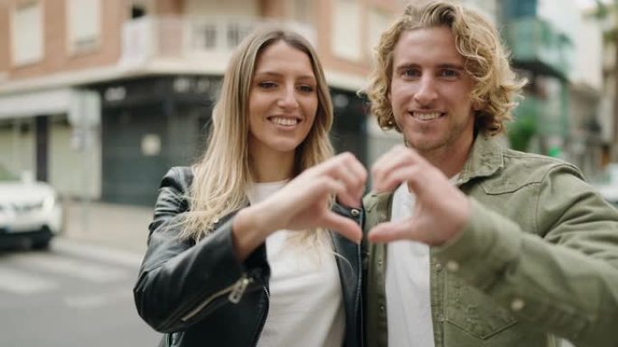 年轻的高加索夫妇微笑着自信地在街上用手做心脏符号