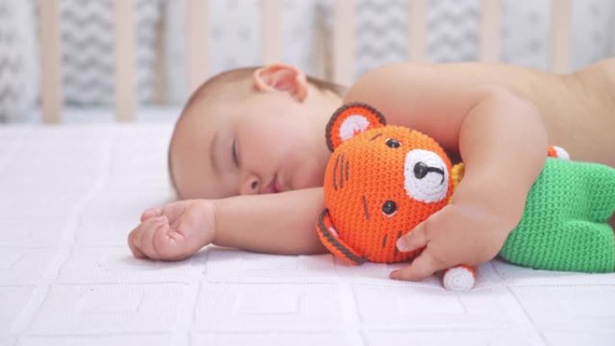 12-17个月大的幼儿睡在床上，抱着一个针织老虎玩具。选择性聚焦。
