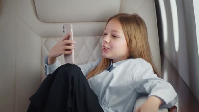 带手机的孩子坐飞机在靠窗的座位上。