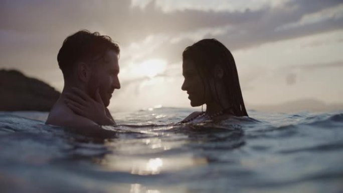 暑假浪漫的异性恋夫妇。在金色日落时在海里游泳。温柔地拥抱