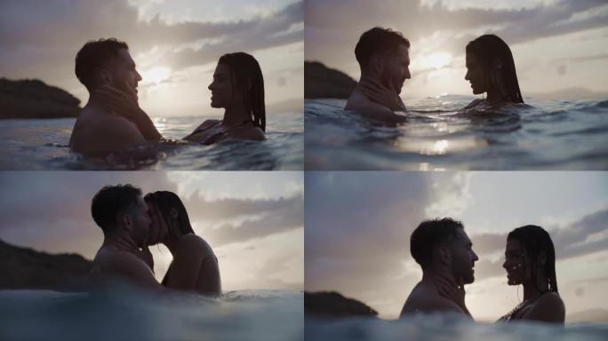 暑假浪漫的异性恋夫妇。在金色日落时在海里游泳。温柔地拥抱