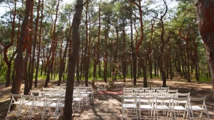 美丽的波西米亚tipi拱形装饰在松树林的户外婚礼场地与锥体。椅子，玫瑰的花卉组合，地毯，串线仙女灯。