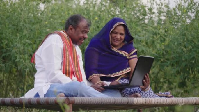中年农村农民夫妇坐在农场里聊天，同时使用笔记本电脑。