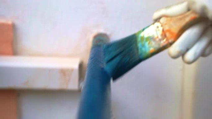 漆刷覆盖蓝色铁管，工人戴着手套油漆金属框架，经过生锈和腐蚀处理。油漆外部金属结构，颜色鲜艳，铁表面修