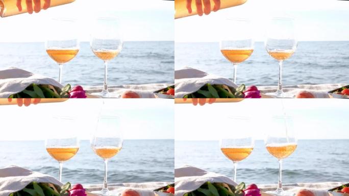 用手将玫瑰酒倒入玻璃杯中，背景是平静的大海。夏季野餐
