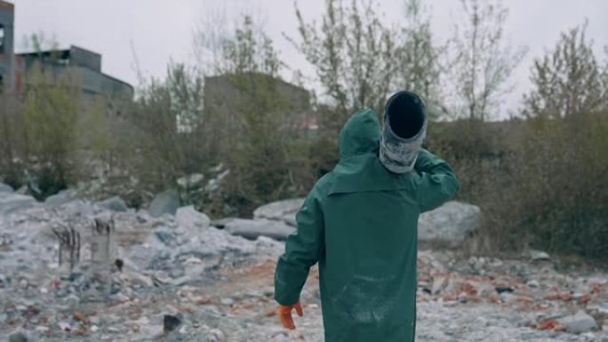 核化学战争后的幸存者。穿着安全服的人在废弃的被污染的地方携带管道在毁坏的建筑物背景上。