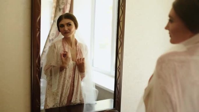 戴着面纱的女孩站在粉色睡衣和缎子长袍照镜子里