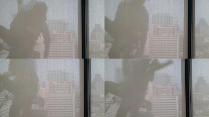 剪影镜头并通过建筑物内部的透明窗帘效果进行拍摄，该人员用擦拭海绵桶的设备清洁高办公楼的窗户，并且存在