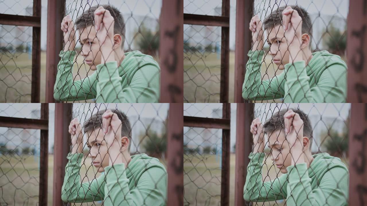 电影难民悲伤的男孩独自一人低头在篱笆附近，沮丧的男孩垂下了眼睛