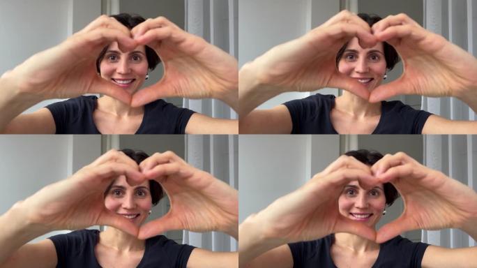 特写快乐微笑的白人种族女人用手指制作心形通过爱的象征看着相机。健康心脏健康人寿保险，爱心慈善，志愿社