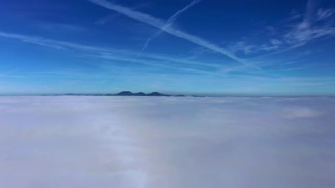 蓝天下的云层的鸟瞰图，背景是山脉，而在雾之间下降
