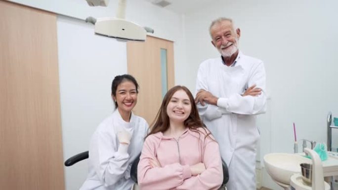 亚洲中年妇女牙科助理、高级牙医和十几岁的女孩病人自信地微笑着，看着相机，在牙科诊所完成牙科护理后，周
