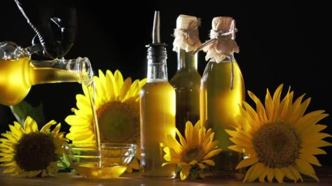 葵花籽油从水罐倒入玻璃碗，一瓶油和黄色的葵花花在附近。碗里流淌着金色的油。太阳的光线穿过油流。玻璃瓶